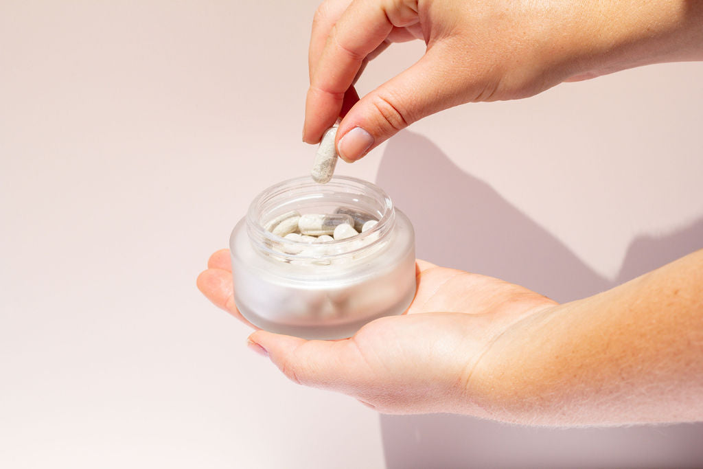 Image of booni doon's CALM Cleansing Capsules jar in a woman's palm with her taking a capsule out